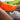 Bright orange sock with blue text, worn on a leg next to a white sneaker. Sunlit background with greenery, conveying a sporty, energetic vibe.